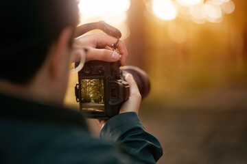 Isolated Close-up of a man holding a modern photo camera while looking at the screen. Horizontal banner image of camera using with the screen visible. Concept of an amateur taking photos in the forest