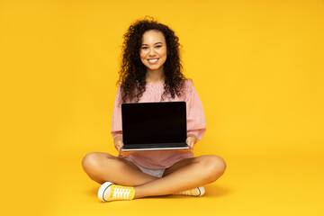 Young attractive girl with a laptop on a yellow background