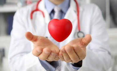 Close-up of male doctor hands holding red heart shape. Medical worker posing in white uniform and stethoscope. Medicine cardiology and healthcare concept