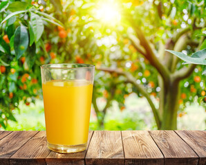 Glass of orange juice on wooden board or table top and blurred orange orchard. Place your product...