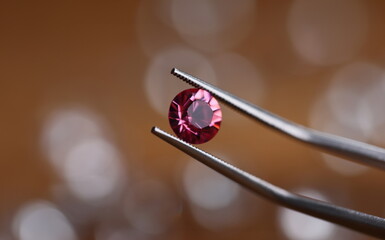Jeweler in workshop holds pink stone in tweezers clamp closeup. Gemstone processing concept