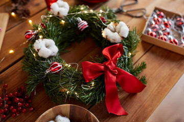 winter holidays, diy and hobby concept - close up of christmas fir wreath and decorations on wooden table
