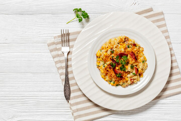 portion of mac and cheese with corn, bacon topped with panko breadcrumbs on white plate on white wooden table with fork, horizontal view from above, flat lay, free space