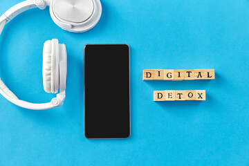 digital detox and technology concept - smartphone, headphones and wooden toy block or stamps on blue background