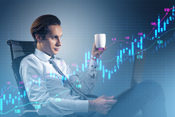 Attractive young businessman with laptop sitting and drinking coffee with glowing upward candlestick forex chart on blurry grid background. Trade, finance and money concept.