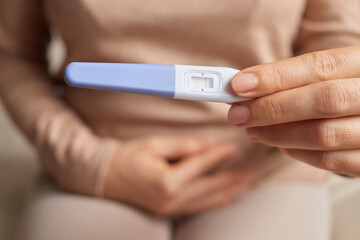 Woman hand holding pregnancy test showing positive result touching her belly waiting for her baby. New life.