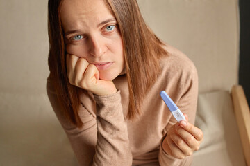 Sad upset unhappy woman hand holding pregnancy test with two stripes positive result future mother...