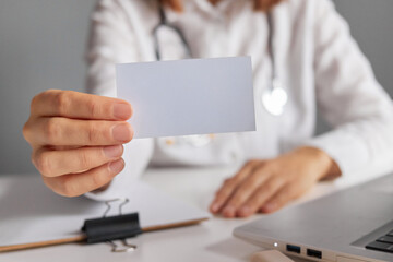 Unrecognizable woman doctor holding empty business or visit card offering her medical services...
