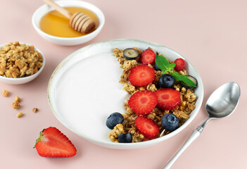 Yogurt bowl with granola and fresh berries: strawberries and blueberries on a pink background. Top view. Copy space.