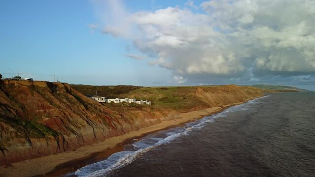 Aerial Drone footage along coast of the Isle of Wight at the Buddle Brock with the cliffs down to the beach. Shot close to sunset and the waves crashing down on the beach and clouds in the sky.