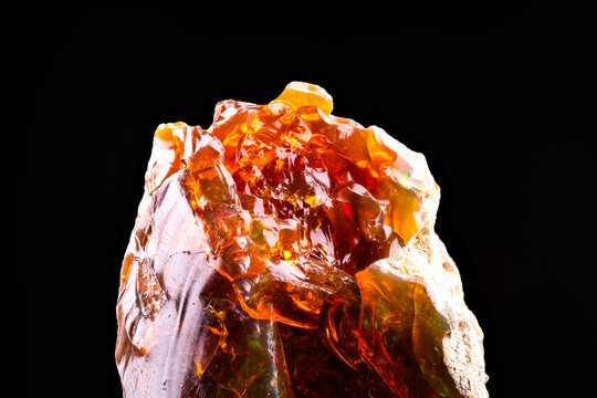 fire opal play-of-color isolated on black background. macro detail close-up rough raw unpolished semi-precious gemstone.
