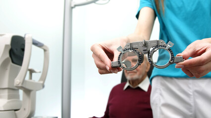 Close-up of glasses for trial optometry in the hands of an ophthalmologist, with an elderly patient...