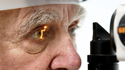 An elderly man in a clinic with an ophthalmologist examines his eyes with a slit lamp and checks...