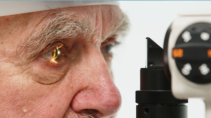 An elderly man in a clinic with an ophthalmologist examines his eyes with a slit lamp and checks...