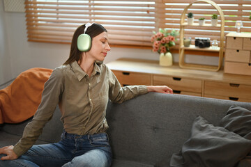 Fototapeta premium Young caucasian woman listening favorite music in headphones, relaxing on couch at home