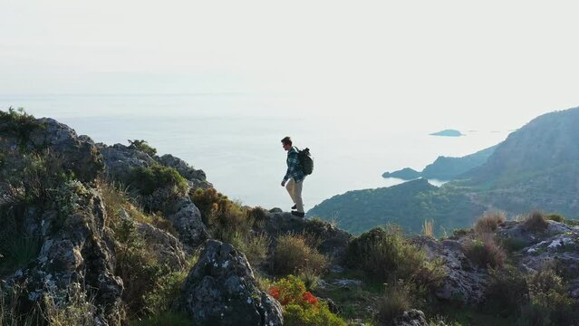 Young man hiking along rocky mountain top with backpack against sky. Side view. Hiking along Lycian path in Turkiye