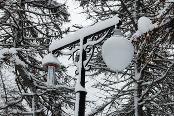 Street light in park with a broken lamp covered with snow. Icicles hanging from the lamps. Picture of winter snowy Magadan city, Russia.