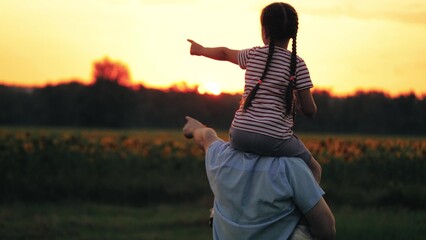 Daughter perches on shoulders of father pointing to sunset and dad follows gaze