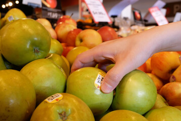 Motion of woman's hand picking organic ambrosia apple inside supermarket