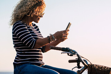 Side view of adult woman using mobile phone connection to messaging sitting on a classic bike. Green transport environment lifestyle. Female people enjoy outdoor leisure and internet connection