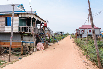 Fototapeta na wymiar Houses made from corrugated iron on wooden stilts in a poor, rural village with a dirt track road in Cambodia.