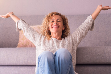 Happy and satisfied woman at home sitting on the floor opening arms and smiling. Concept of joyful lifestyle female people. Indoor leisure activity, Success and enjoying lifestyle. Indoor apartment - obrazy, fototapety, plakaty