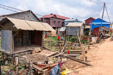 Houses made from corrugated iron on wooden stilts in a poor, rural village with a dirt track road in Cambodia.