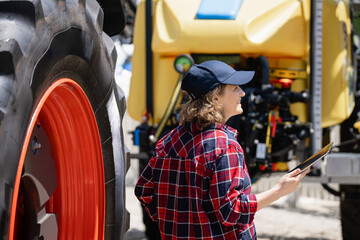 Female farmer with a digital tablet next to agricultural tractor.