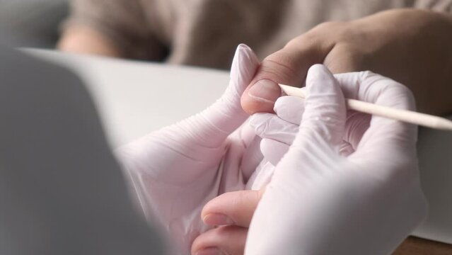Close up of hands of professional salon worker holding client hand while using cuticle pusher. Process of manicurist using cuticle pusher when working with girl client. Nail technician working.