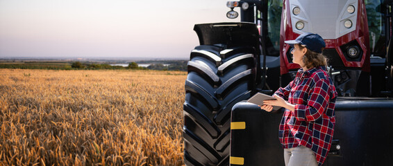 Female farmer with a digital tablet next to agricultural tractor.