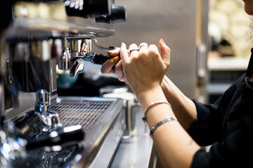 An unrecognizable female waitress is attaching a portafilter to a professional coffee maker to make a coffee inside a restaurant. Concept of filtering coffee, portafilter on coffee machine.