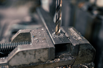 Close-up of a metal bar in a clamp and a drill bit, drilling a hole in a metal rod