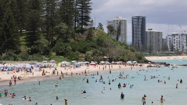 A bustling beach filled with people swimming and enjoying summer activities in Australia's Gold Coast.