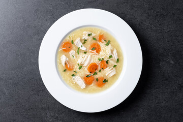 Chicken soup with vegetables on black background. Top view