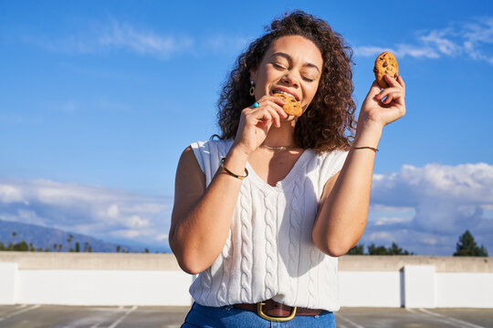 Woman eating cookie outdoors taking bite holding cookie in each hand