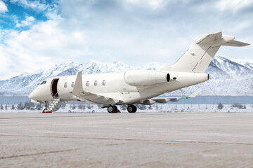 Modern white business jet with an opened gangway door at the winter airport apron on the background of high scenic snow capped mountains