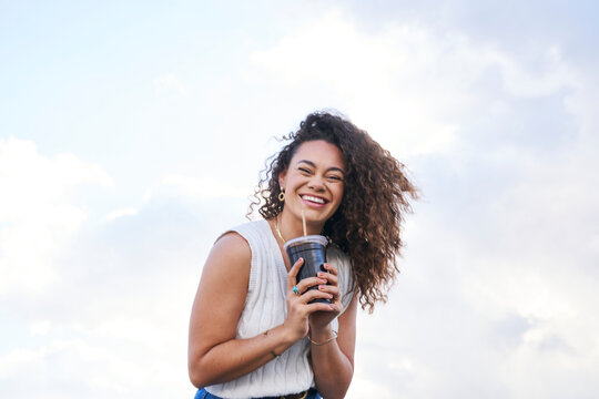 woman enjoying soft drink outdoors smiling at camera and holding drink in both hands