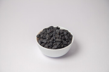 Dried black raisin on white bowl with white background, Dried black raisin scattered on the white background in a black bowl or vessel