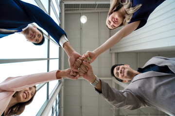 Team building concept. Coworker standing in circle bumping fist together, celebrating business success in modern office with high ceiling. Bottom View - obrazy, fototapety, plakaty