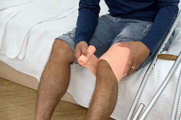 A man with a broken knee sitting on his bed. He leans on crutches, signalling recovery from injury....
