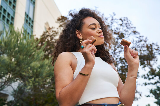 Woman eats fig bar by trees and lavender holding two bars