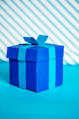 Blue handmade paper gift box with bow on blue background with stripes