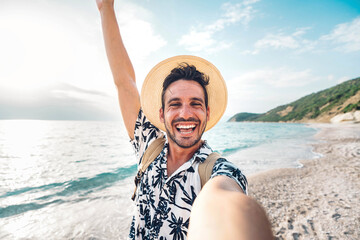 Handsome young man taking selfie picture with smart mobile phone outside - Happy tourist enjoying summer holiday at the beach - Traveling and technology life style concept - obrazy, fototapety, plakaty