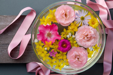 Runde Wasserschale mit schönen Blüten in rosa und gelb auf grauem Holz mit glänzendem...