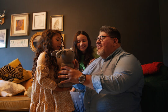Father sitting in living room with his daughters playing with toy bunny smiling
