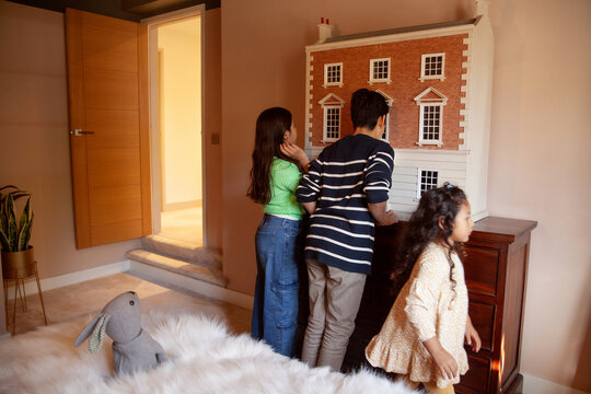 Three siblings looking at toy doll house in bedroom
