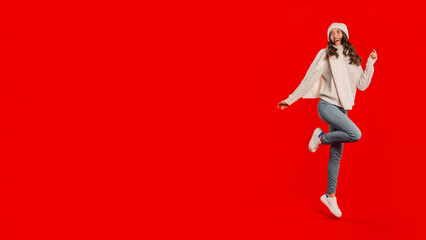 Joyful young European lady in knitwear dances on red background