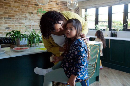 Happy mother handing sandwich to daughter with down syndrome in kitchen