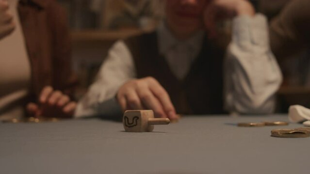 Close-up shot of hand of unrecognizable Jewish woman spinning wooden dreidel toy on table during Hanukkah festival, with visible Hebrew letters Shin - put in gelt coin, and Nun - nothing