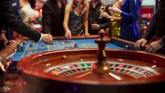 Anonymous Group of Elegant Casino Guests Placing Bets on a Table. Focus Switching to a Close Up Footage of a Spinning Roulette Wheel with a Ball Stopping at Number One Red